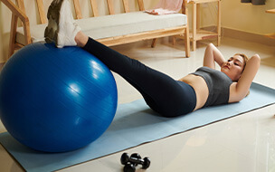 Young woman doing crunches with legs on fitness ball when exercising at home