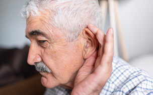 Senior man suffering from deafness cupping his hand up to his ear