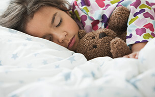 Mixed race girl sleeping in bed with teddy bearv
