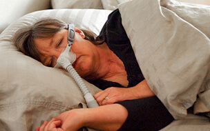 Middle aged woman with Sleep Apnea in bed wearing a CPAP machine