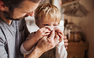 A young boy holds a tissue as he sneezes