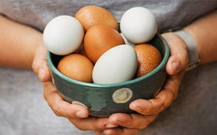 A woman holding a bowl with fresh brown and white eggs