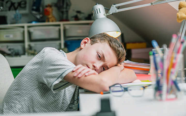 young boy at desk with head resting on folded arms