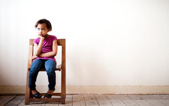 A young girl sitting on a chair in an empty room