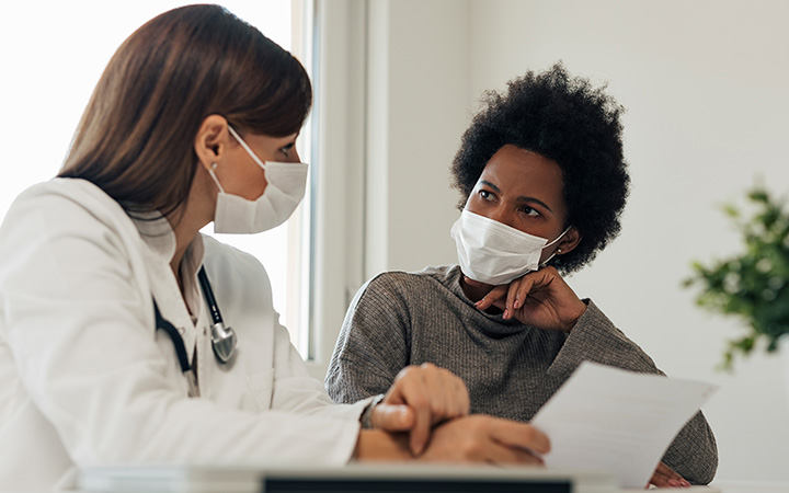 Masked physician consults with masked patient