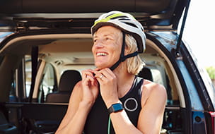 older woman fastening bike helmet while seated in open car hatchback