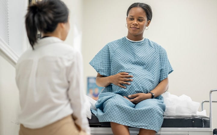 A young pregnant woman sit up on an exam table in her doctor's office during a routine prenatal check-up
