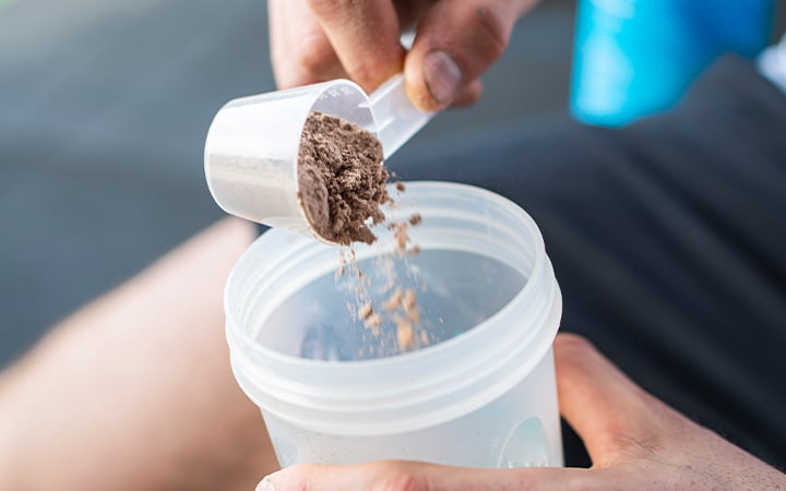 Sportsman putting protein powder in shaker after working out