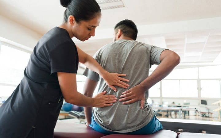 A female massage therapist massaging a male patient’s back with both hands