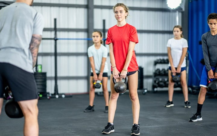 A group of children work out together in a gym with kettlebells