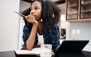 A young girl looking unhappy while doing a school assignment at home