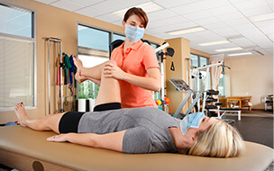 Physical therapist wearing protective face mask evaluates range of motion on female patient