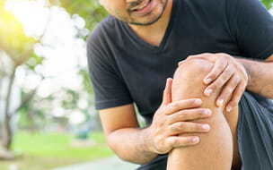 A young male holding his injured knee during exercise in the park