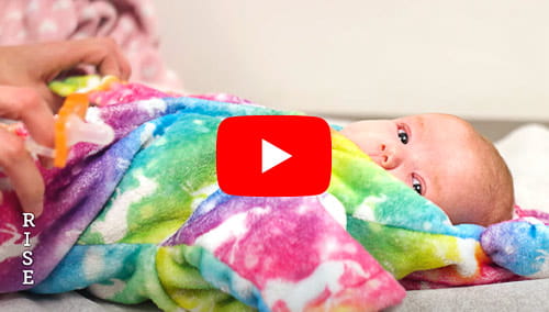A baby rests underneath a colorful blanket