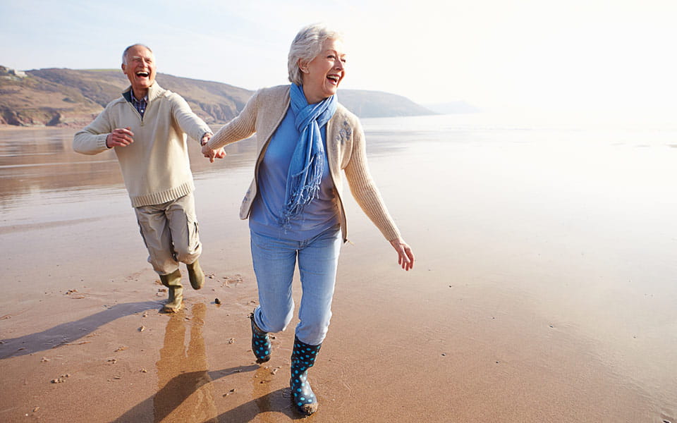 Senior couple running along winter beach laughing