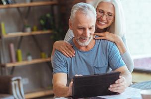 Older man uses tablet as wife looks on, smiling