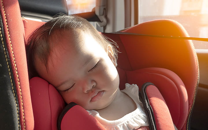 A baby girl sleeping on her car safety seat with sunlight through the window