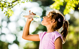 young girl in pink top drinking glass of water with trees in the background