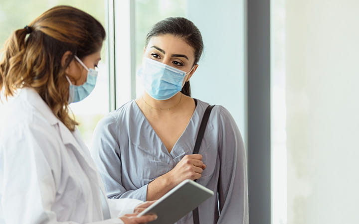 masked female physician conferring with young masked female patient