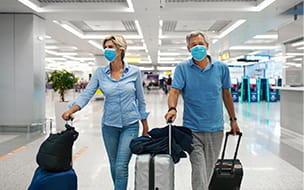 masked couple in blue walking through airport with roller luggage