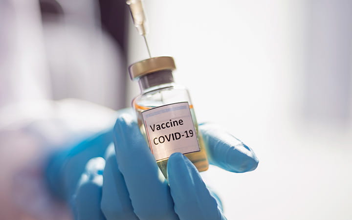 gloved hand holding covid vaccine vial