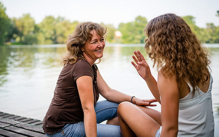 A cheerful mother and daughter sitting on the edge of a wooden jetty