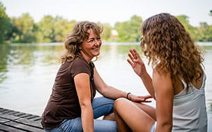 A cheerful mother and daughter sitting on the edge of a wooden jetty