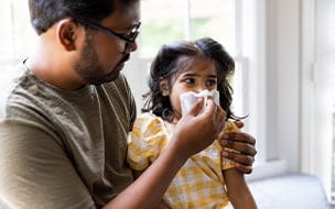 A father wiping his toddler daughter's nose