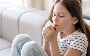 A young girl sitting on a sofa, feeling bad and suffering from dry cough
