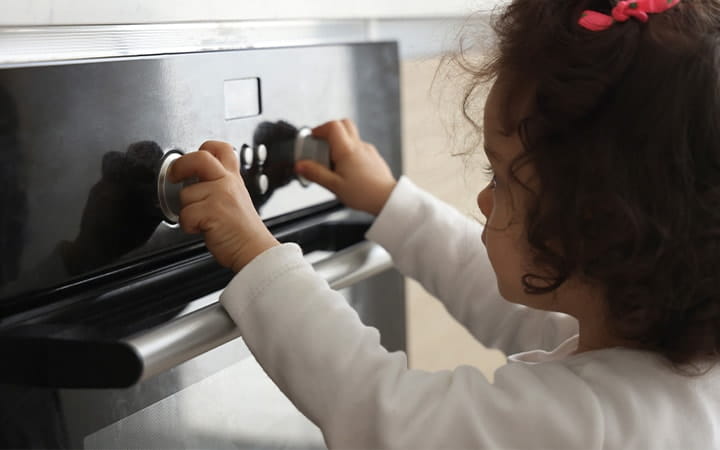 A little girl turns knobs on an oven