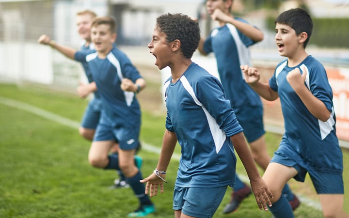Energetic preteen and teenage male footballers cheering and punching the air as they run onto field for training session