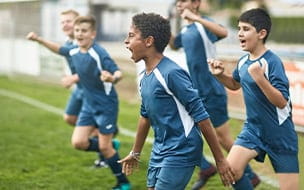 Energetic preteen and teenage male footballers cheering and punching the air as they run onto field for training session