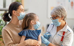 A doctor vaccinating a young girl, who is being held by her mother