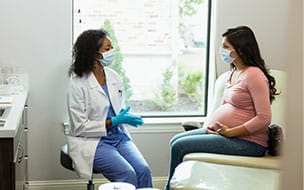 A female doctor and a pregnant woman are both wearing protective masks during a prenatal medical exam