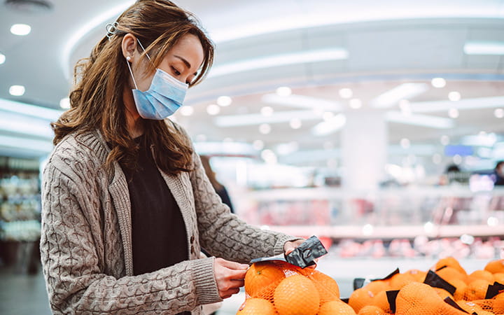 woman wearing mask shopping for oranges