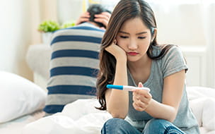 woman looking at home pregnancy test with man next to her with head in hands