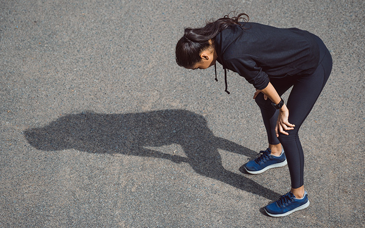 woman runner throws a shadow as she hunches over on her knees 