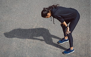 woman runner throws a shadow as she hunches over on her knees 
