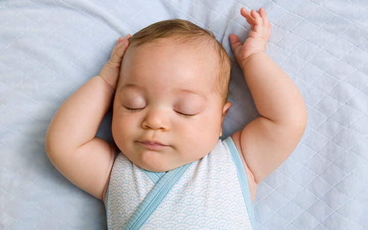 young infant lying on back with arms overhead