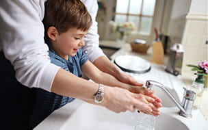 A four year old boy washing the dishes with his mum in the kitchen