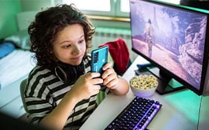 A young child using a smart phone while playing video games on a PC
