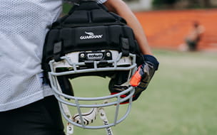 A boy holds a football helmet equipped with a Guardian Cap