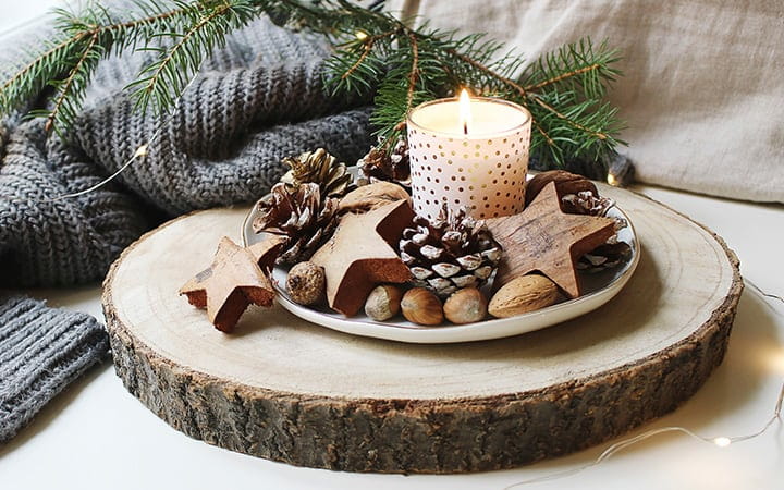 Burning candle decorated by wooden stars, hazelnuts and pine cones standing near window on wooden cut board