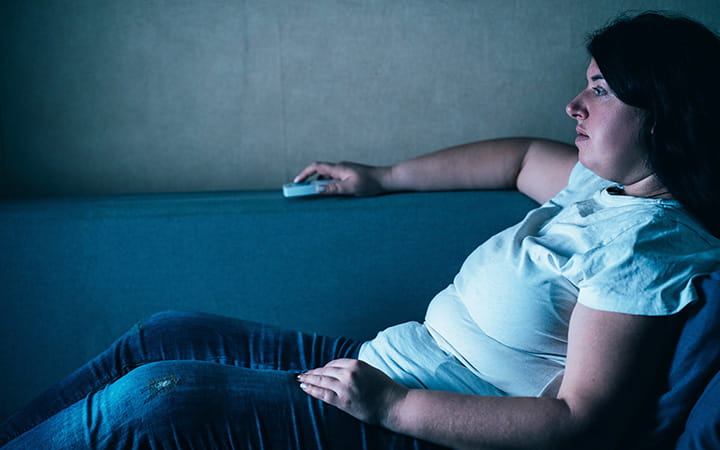 Overweight woman lies on couch with remote