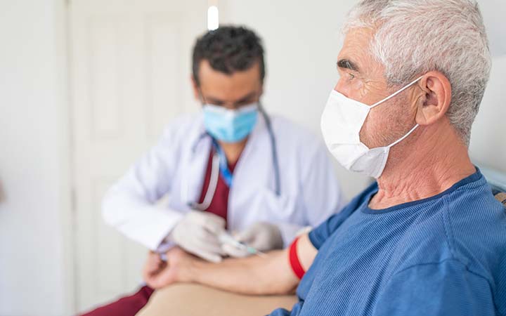 male doctor in mask drawing blood from older male adult