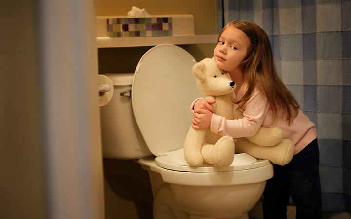 young girl hugs teddy bear that sits on toilet