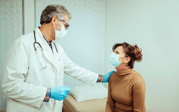 masked male doctor with reassuring hand on masked female patient's shoulder
