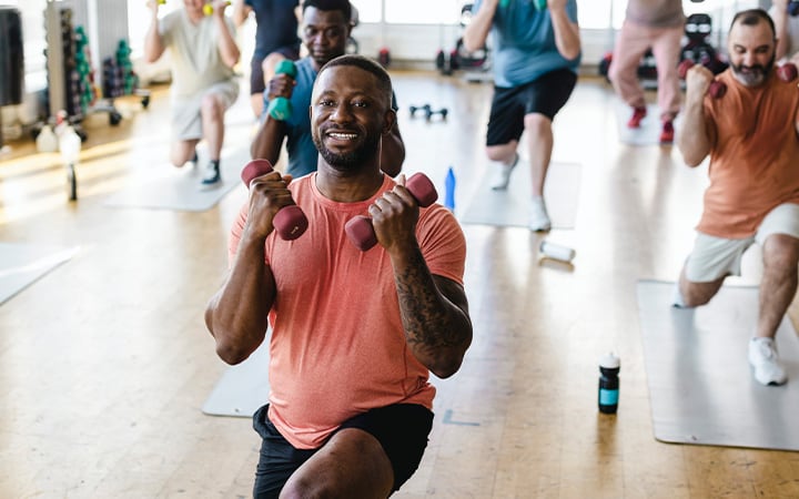 Smiling male fitness instructor practicing dumbbell exercise with men in gym
