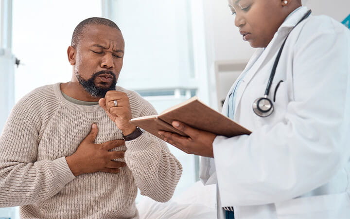 A mature man coughing during a consultation with a doctor in a clinic