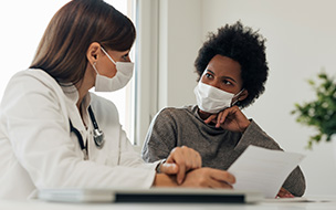 Masked physician consults with masked patient